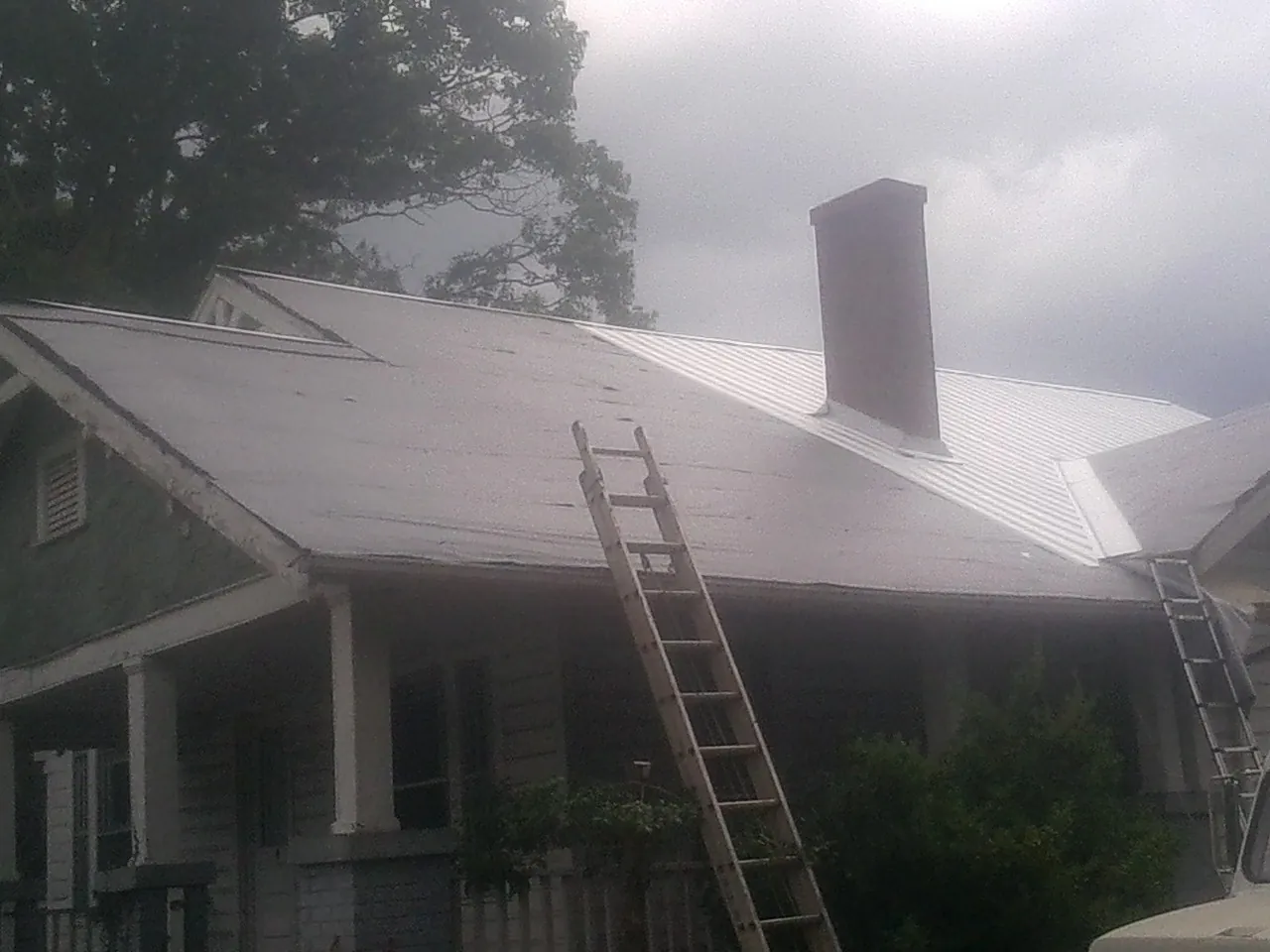 Ladders against a metal roof on an older home with a brick chimney in Milford